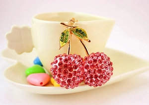 Macro shot of cherry keychain with pink rhinestones and green leaf on a gold metal frame