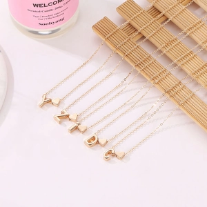 Golden heart pendant necklace with initial letters on a bamboo coaster, lifestyle shot