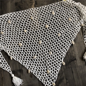 Detalle de chal de playa de ganchillo blanco con conchas y flecos sobre fondo de madera