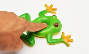 Close-up of hand squeezing elastic green frog toy with yellow belly and red eyes