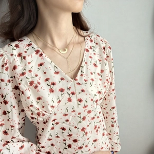 Detailed view of layered gold necklace worn with a V-neck red floral print dress