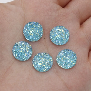 Close-up of five blue 12mm sparkling resin druzy cabochons held in a hand for scale