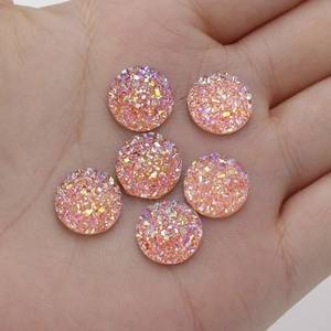 Close-up of 12mm round resin rhinestones with pink orange iridescent sparkle in hand