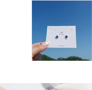 Detailed view of blue planet and moon stud earrings held against a clear blue sky