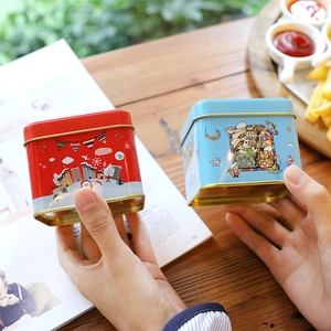 Square Christmas tin boxes in red and blue with festive snowman and house illustrations