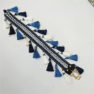 Détail d'une bandoulière tissée style bohème avec pompons bleus et crochets dorés