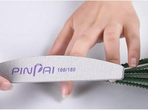 Close-up of double-sided 100/180 grit half-moon nail file polishing a fingernail surface
