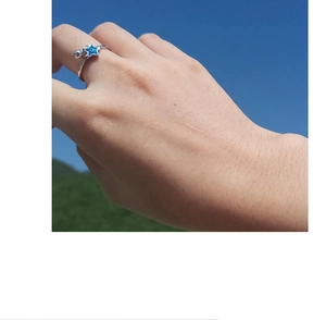 Detail of silver star ring with blue star charm and bead worn on finger with sky backdrop