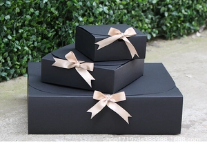 Three sizes of black gift boxes with champagne bow ribbons stacked in outdoor setting