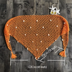 Detalle de chal playero de ganchillo naranja con conchas naturales y borlas finas