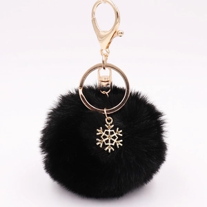 Macro detail of black faux fur pompom and golden snowflake alloy charm on keychain