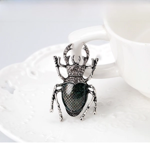 Detail of vintage beetle brooch with crystal pavé and green textured abdomen on lace tray
