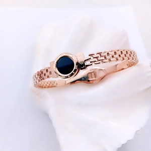 Detail view of rose gold stainless steel bracelet with black roman numeral disk and LOVE engraving