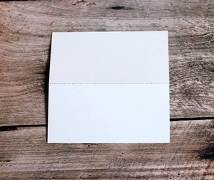 Macro detail of white square place card with dotted fold line on dark wood background