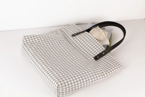 Detail of gingham tote bag featuring durable leather straps and gold metal rivets