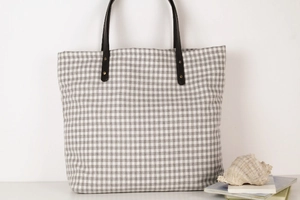 Detail of grey checkered canvas tote bag with black leather handles and metal rivets