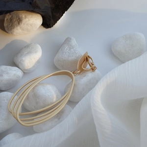 Macro detail of golden matte multi-layer geometric oval clip earrings on white stones