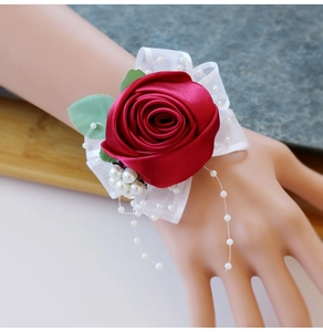 Close-up of deep red satin rose wrist corsage with lace straps and pearl beads