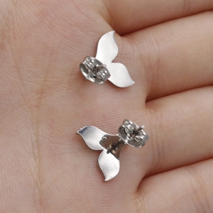Polished silver mermaid tail stud earrings in stainless steel held in palm for scale