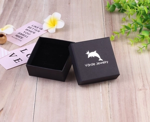 Macro view of square black jewelry box with silver logo on light wood background