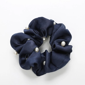 Détail d'un chouchou en satin bleu foncé avec perles blanches sur fond blanc pur