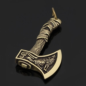 Detail of brass viking axe pendant with wolf relief and textured handle on reflective surface