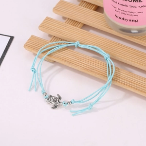 Detail of a handmade blue rope anklet featuring a silver sea turtle charm and beads