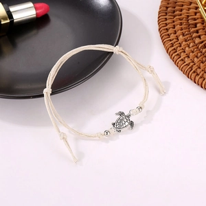 Detail of hand-woven beige rope anklet featuring an antique silver turtle charm pendant