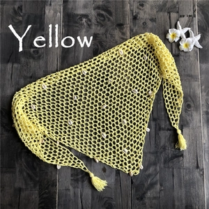 Detalle de chal playero de ganchillo amarillo con borlas de conchas sobre fondo de madera