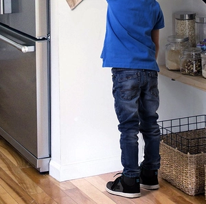 Kid wearing blue t-shirt and denim jeans standing in a bright minimalist kitchen