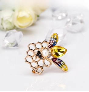 Macro shot of bee brooch with yellow crystal, pearl head and enamel honeycomb details