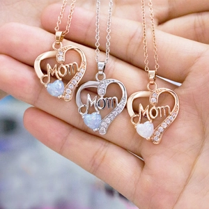 Silver heart pendant necklace with opal and Mom lettering held in hand for scale