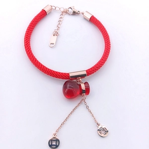 Detail of red braided cord bracelet featuring a rose gold money bag charm and coins