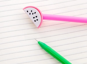 Close-up of watermelon-shaped gel pens writing on lined notebook paper