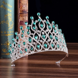 Elegant silver crown with green teardrop crystals and rhinestones on a wooden surface