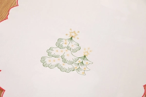 Detail of Christmas table runner featuring green tree embroidery and red scalloped edges