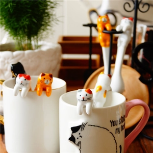 Detail shot of cute 3D ceramic cat spoons hanging on mugs for kitchen coffee stirring