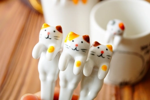 Close-up of hand-painted ceramic cat-shaped spoons hanging on a white ceramic mug rim