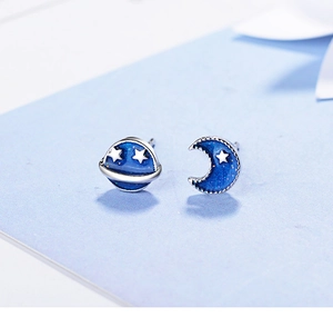 Detailed close-up of blue planet and crescent moon stud earrings with silver sparkles