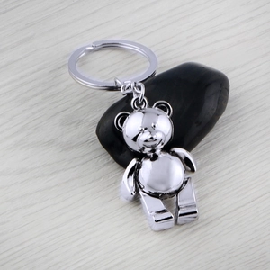Polished silver teddy bear keychain on black stone with minimalist wood background