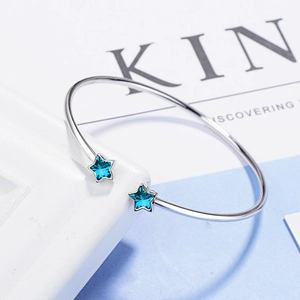 Minimalist silver open bangle with two blue star crystals on a white geometric prop