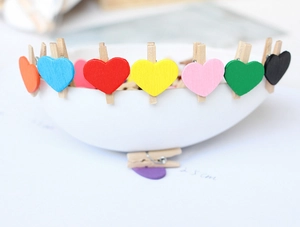 Close-up of colorful wooden heart clips on white bowl edge with shallow depth of field