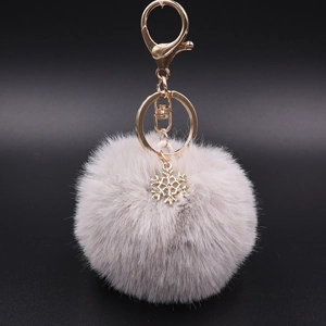 Detailed view of grey plush pompom keychain with golden snowflake charm and lobster clasp
