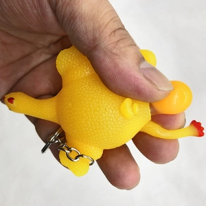 Close-up of hand squeezing yellow rubber chicken keychain toy to pop out an egg