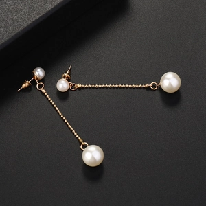 Detail of long gold earrings with large and small pearls on a textured black surface