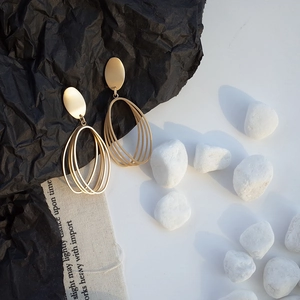 Detail of matte gold geometric oval earrings with nested ring pendants on black and white stone