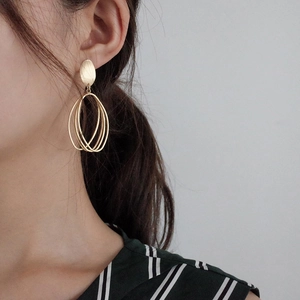 Close-up of matte gold geometric multi-layer oval drop earrings on a model