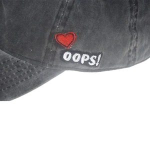 Close-up of red heart embroidery and 'oops!' patch on washed cotton baseball cap