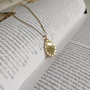 Macro detail of golden oval pendant with scalloped edges on vintage book pages