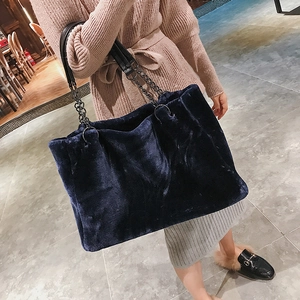 Detail of dark blue plush tote bag featuring a metal chain strap in a cozy cafe setting